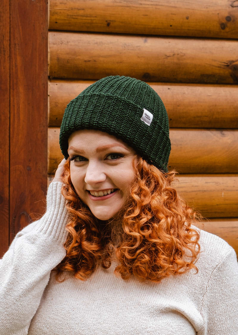 model with red hair smiling and wearing the forest green beanie by mimi and august 