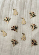 Ten pear and olive branch enamel pins from Mimi & August are displayed on a light fabric background—perfect for your collection or as a gift. Get them as Free Enamel Pins (100% off) in the BOGO Bundle at BOGOS.io.