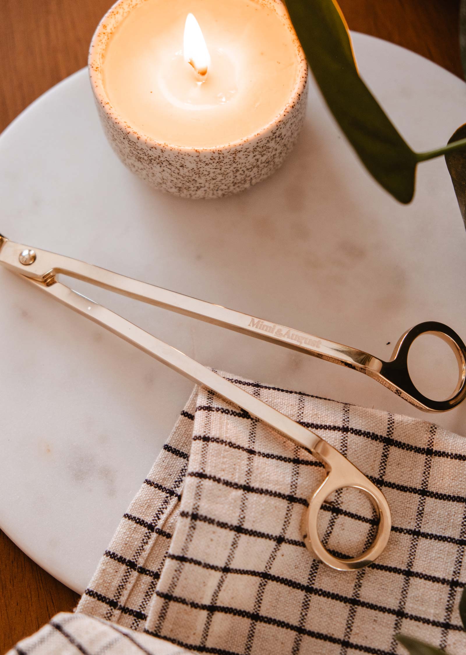 Une paire de coupe-mèches durables Mimi et August repose sur une table à côté d’une bougie réutilisable.