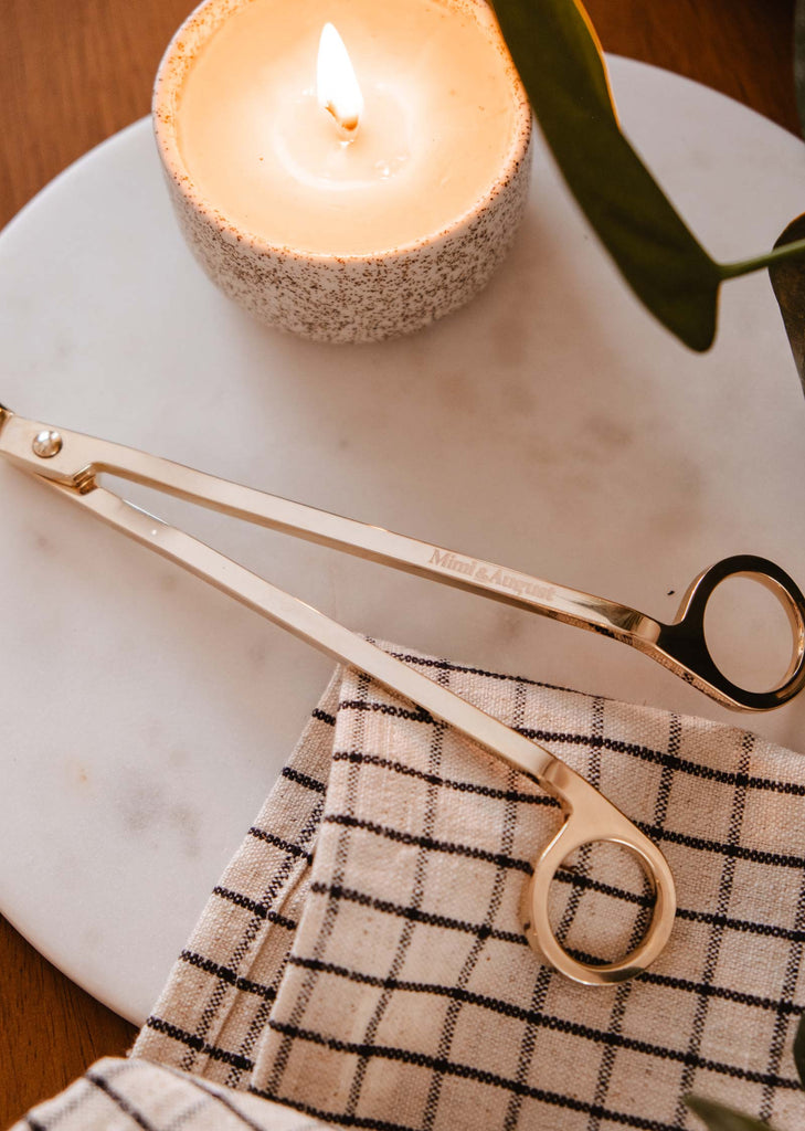 A durable pair of Mimi & August Wick Trimmers sit on a table next to a reusable candle.