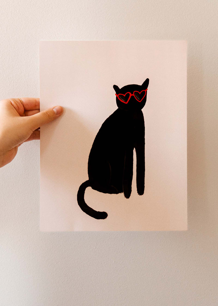 Une affiche excentrique Mimi & August représentant une personne tenant une affiche avec un chat noir avec des lunettes.