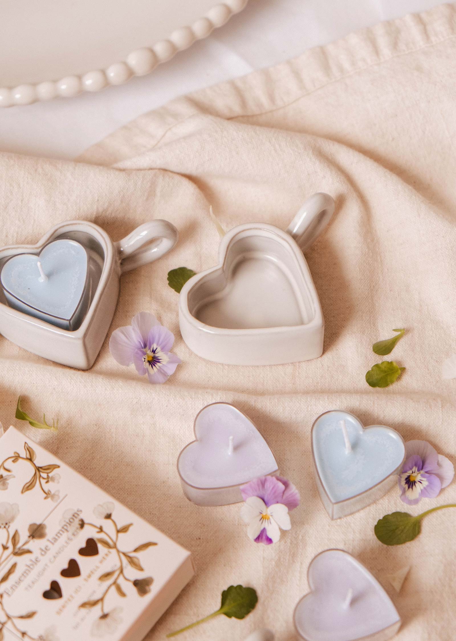 Le porte-bougies à réchaud Heart & Glow de Mimi & August est présenté sur un tissu avec des fleurs délicates et une boîte décorative, créant ainsi un charmant présentoir sur le thème du cœur.