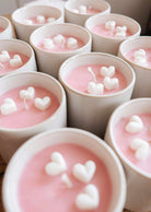 The Special Edition Candle by Mimi & August features white cups filled with pink wax and topped with small white heart-shaped decorations, bringing a charming touch to any space.