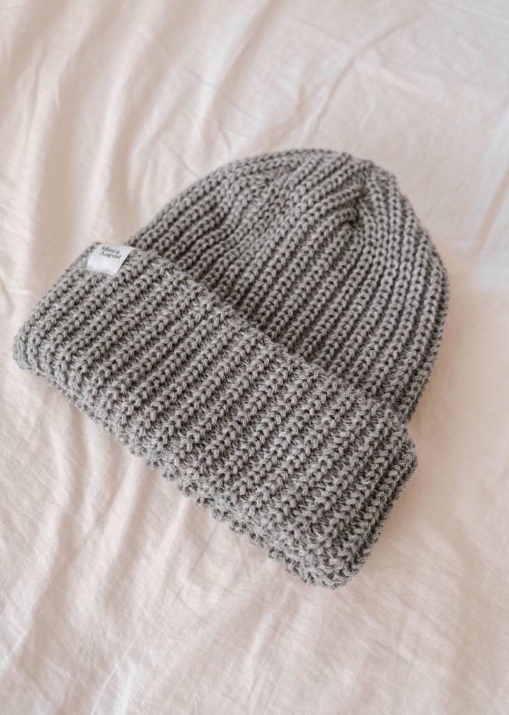 Le bonnet Chunky gris chiné de Mimi & August, fabriqué à partir d'un fil chunky et doté d'un bord plié, repose à plat sur une surface blanche. Cet accessoire d'hiver douillet est parfait pour les journées fraîches.