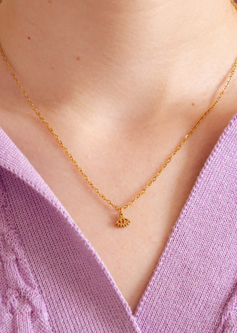 A close up of a person wearing a Mimi and August gold plated necklace with Eye of Horus pendant