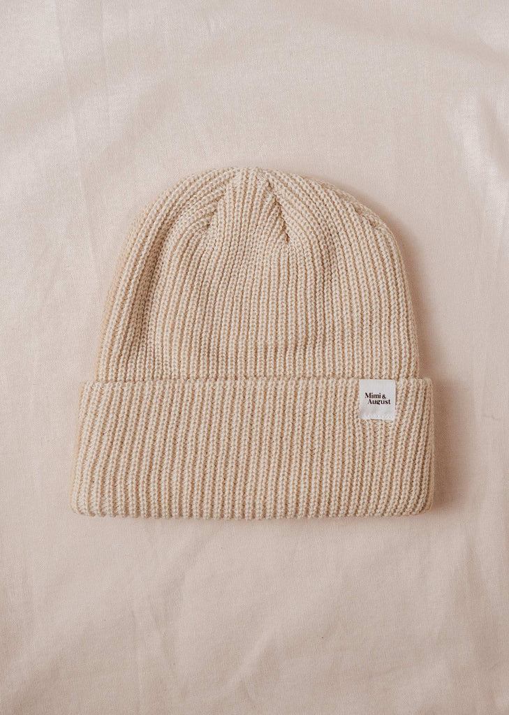 An Ivory Cuffed Beanie in beige on a bed by mimi and august.