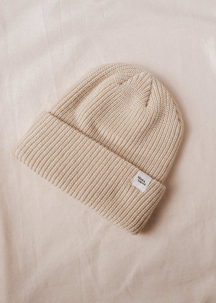 An Ivory Cuffed Beanie in beige on a bed.