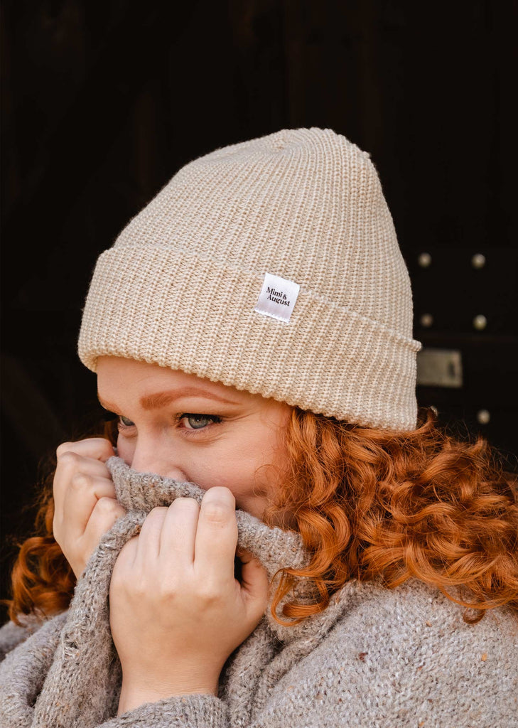 A woman wearing an Ivory Cuffed Beanie from mimi and august and a scarf.
