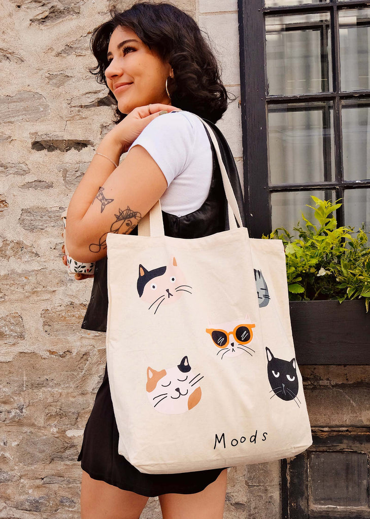 A woman stylishly holding a tote bag adorned with adorable illustrations of cats.