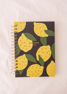 Introducing the Lemon - Agenda 2025 by Mimi & August: a chic planner featuring a hand-drawn lemon pattern with vibrant yellow lemons and lush green leaves set against a dark background.