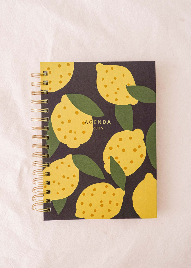 Voici le Lemon - Agenda 2025 de Mimi & August : un agenda chic avec un motif de citron dessiné à la main avec des citrons jaunes vibrants et des feuilles vertes luxuriantes sur un fond sombre.