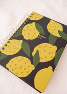 The Lemon - Agenda 2025 by Mimi & August, featuring a vibrant hand-drawn lemon pattern and a spiral binding, rests gracefully on a light surface.