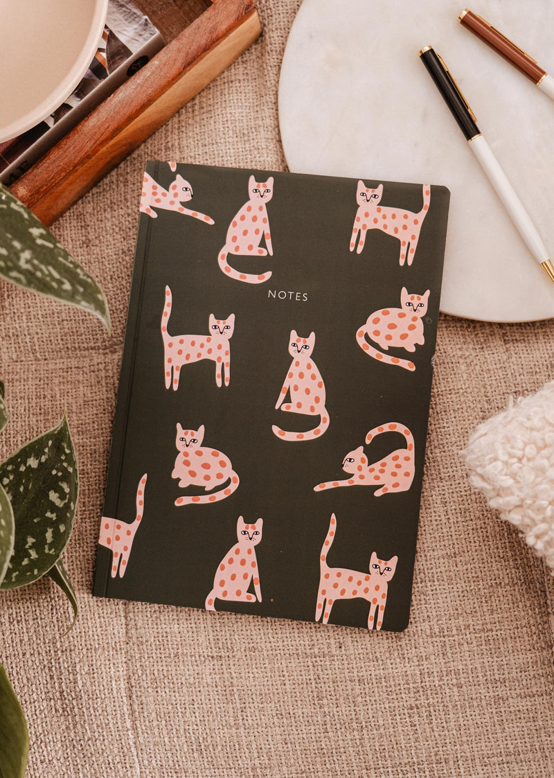 Mimi & August's Leo the cat Notebook, a beloved companion for cat lovers, adorns a charming notebook nestled alongside a vibrant plant.