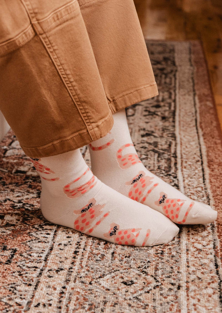 A cat lover wearing a pair of Mimi & August Leo The Cat Socks, featuring a pink flower, for everyday wear.