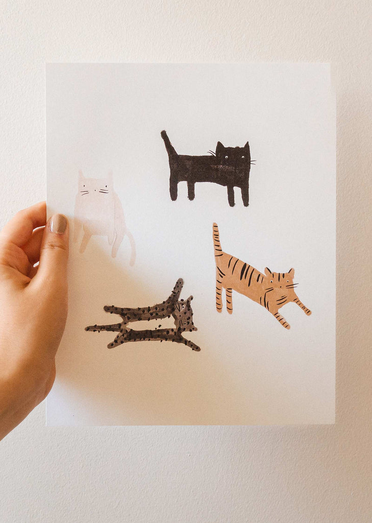 Une personne tenant une illustration avec quatre chats dessus par mimi et august