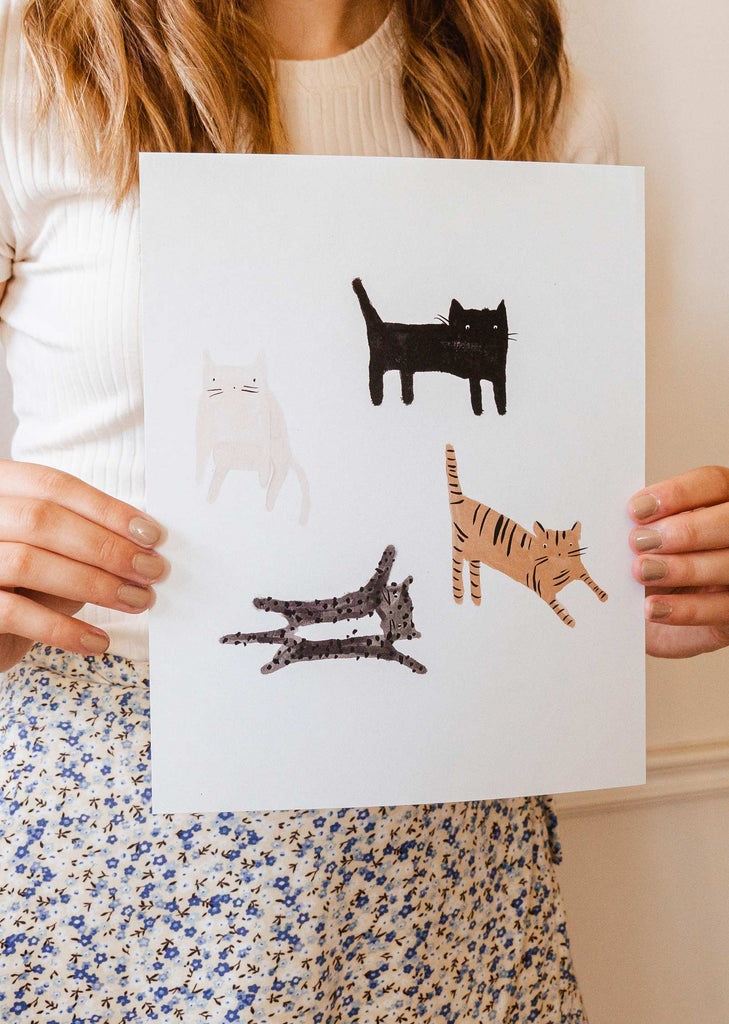 A girl holding up an illustration about four funny cats on it.