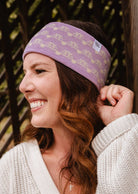 Woman with wavy brown hair wearing a Mimi & August Lilac Bliss Headband and cream sweater, smiling and looking to the left.