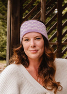 A woman with long wavy hair wearing a pink Mimi & August Lilac Bliss Headband and a white sweater, the perfect cold-weather essential, smiles in an outdoor setting.