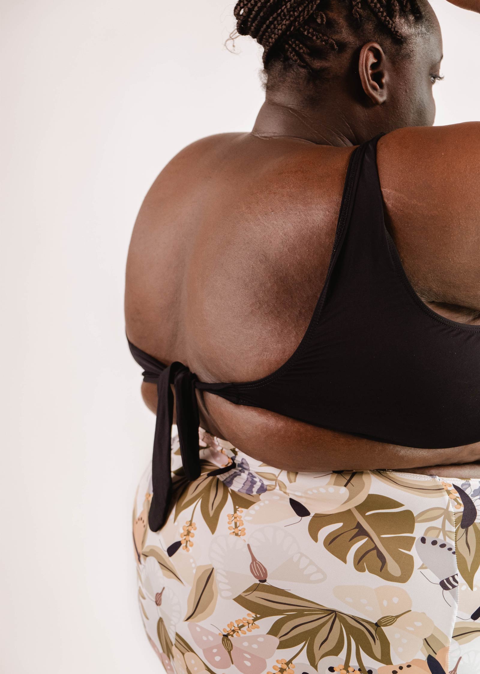 A person is shown from the back wearing a Mimi & August Lima Black Bralette Bikini Top with an adjustable back, paired with patterned bottoms featuring floral designs.