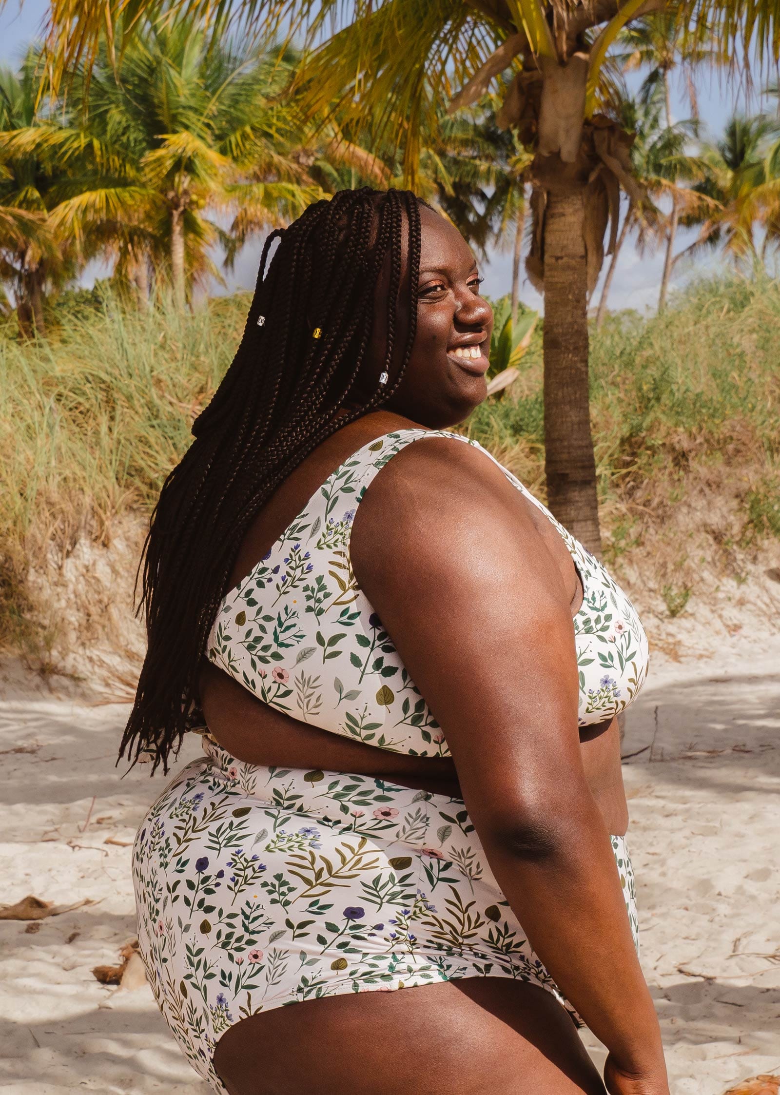 Une femme vêtue d'un haut de bikini mimi et august Lima Herboria Bralette, avec des couleurs blanches et vertes, debout sur une plage.