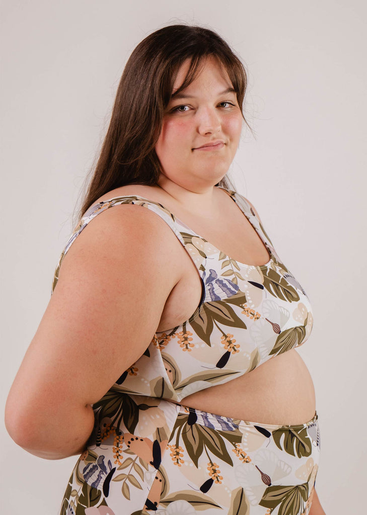 A person in a floral-patterned Lima Mariposa Bralette Bikini Top by Mimi & August with an adjustable back stands against a plain background, exuding comfort and confidence.