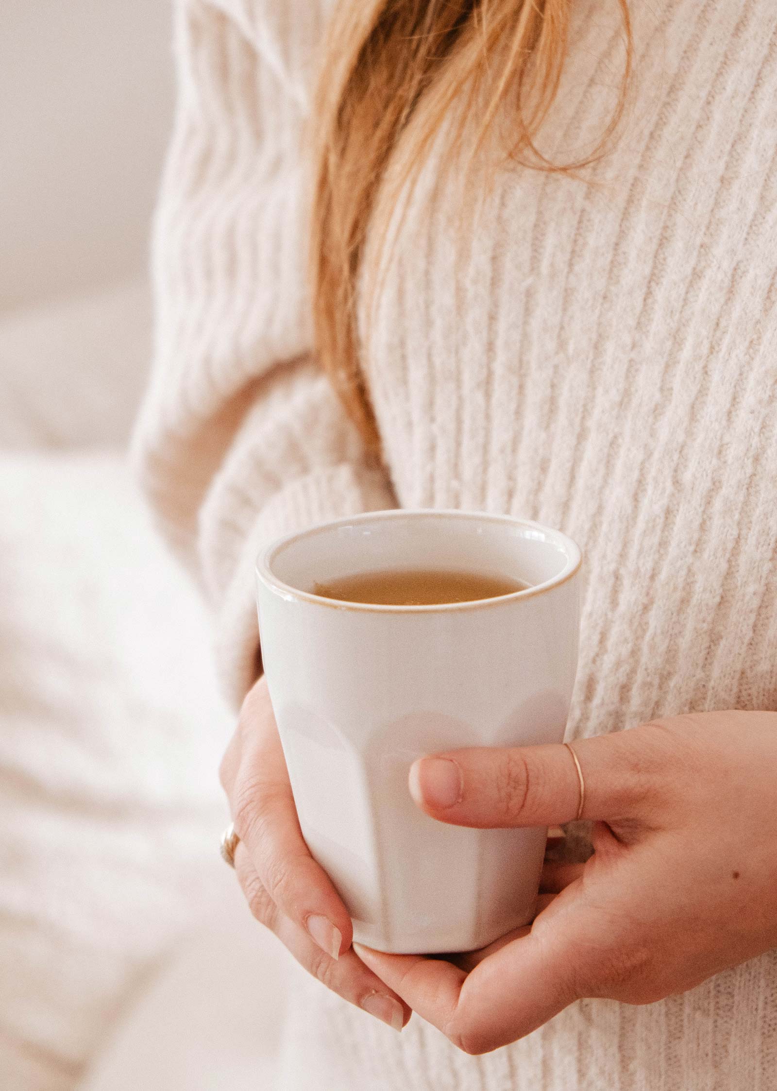 Une personne vêtue d'un pull-over crème tient la tasse en céramique Mimi & August's Douceur du matin, remplie d'une boisson chaude.