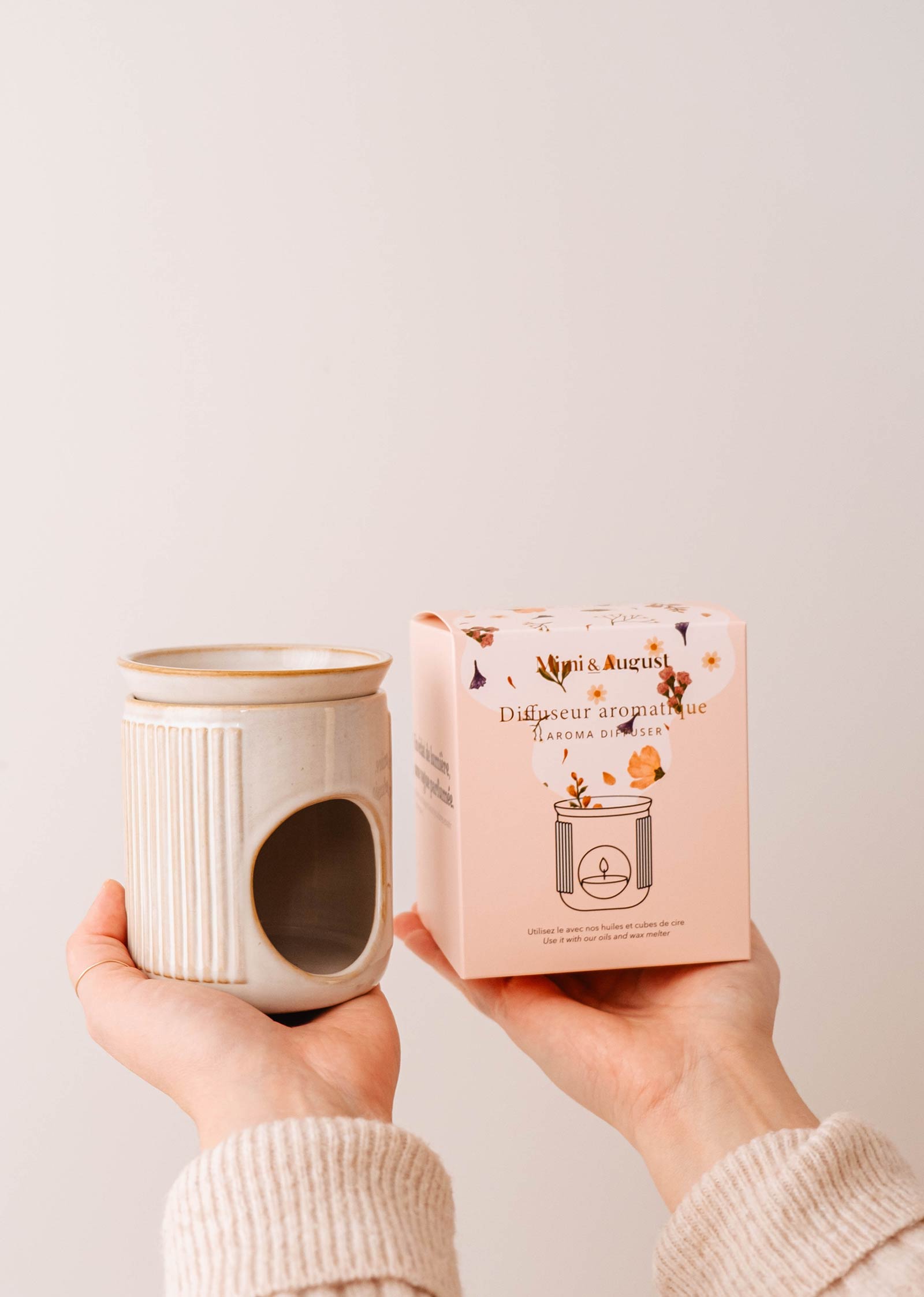 Hands holding the Lueur – Aromatic Ceramic Diffuser and a pink floral design box, ideal for pairing with scented oils from Mimi & August.