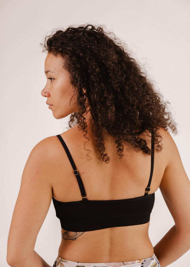 Person with curly hair wearing a Mimi & August Mango Black Bralette Bikini Top with adjustable straps, viewed from the back and slightly to the side against a plain background.