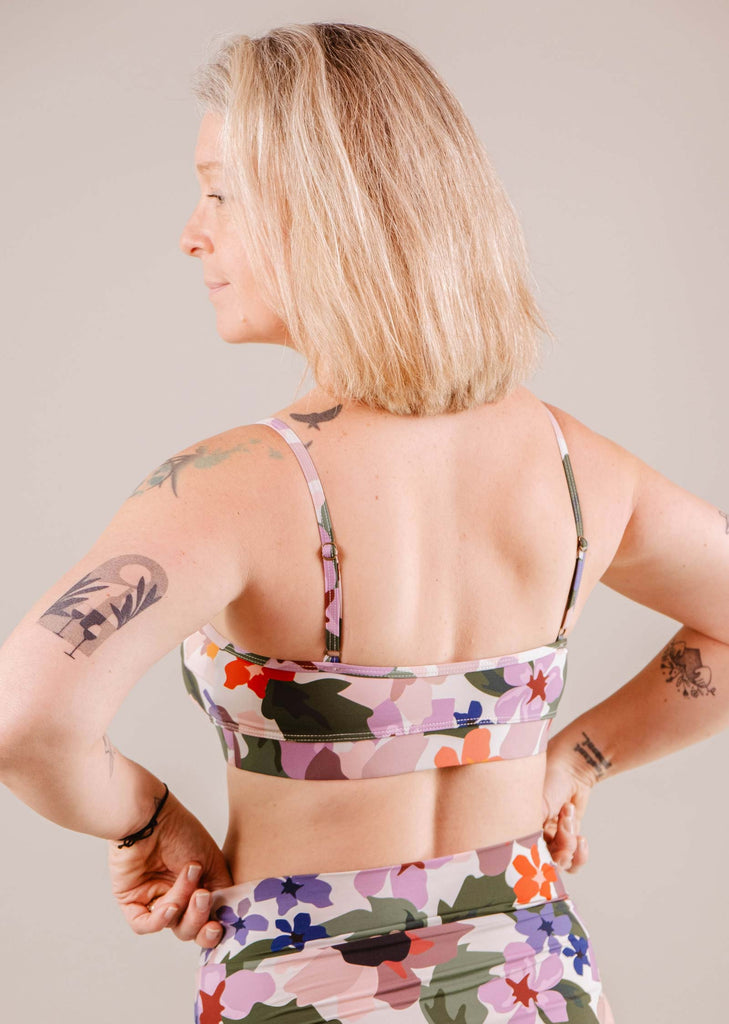 Woman in floral Mimi & August Botanica Bralette Bikini Top and leggings, viewed from the back, displaying tattoos on her arms and back.