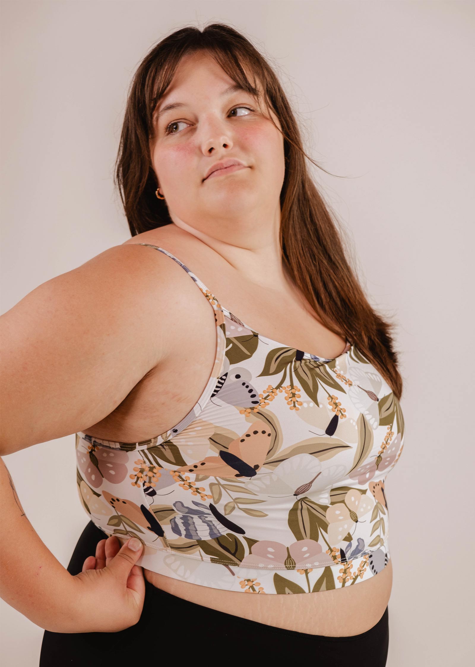 A person in a Mango Mariposa Bralette Bikini Top by Mimi & August with adjustable straps looks to the side, standing against a plain background.