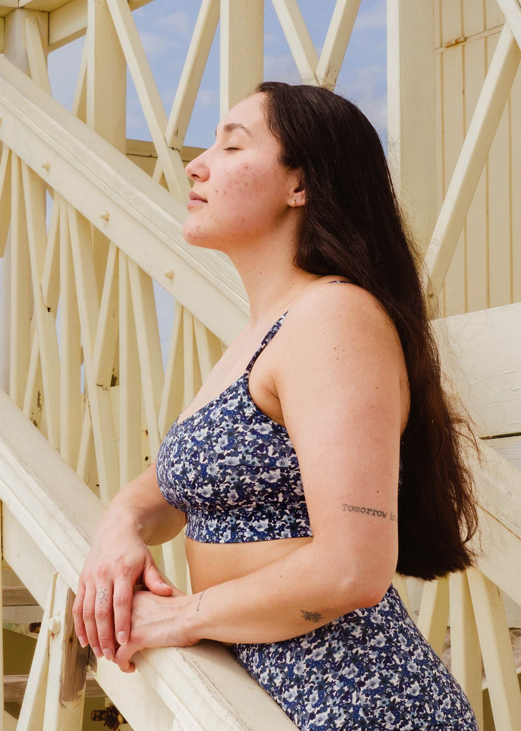 A woman leaning on a staircase with her eyes closed wearing the Mango Moonflower Bralette bikini top by mimi and august.