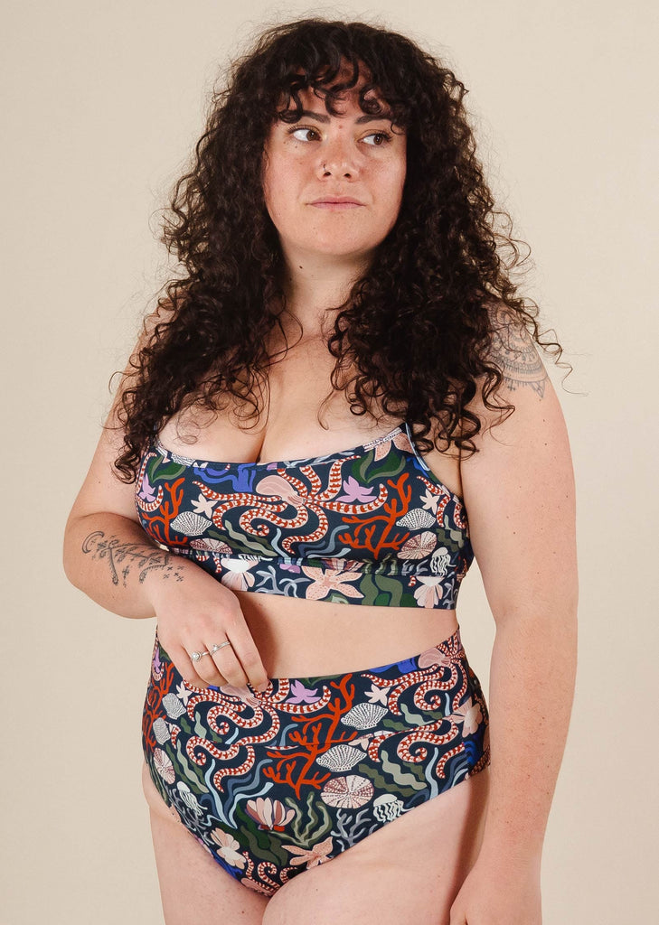A woman with curly hair wearing a comfortable Coral Bikini Sea Print top from mimi and august.