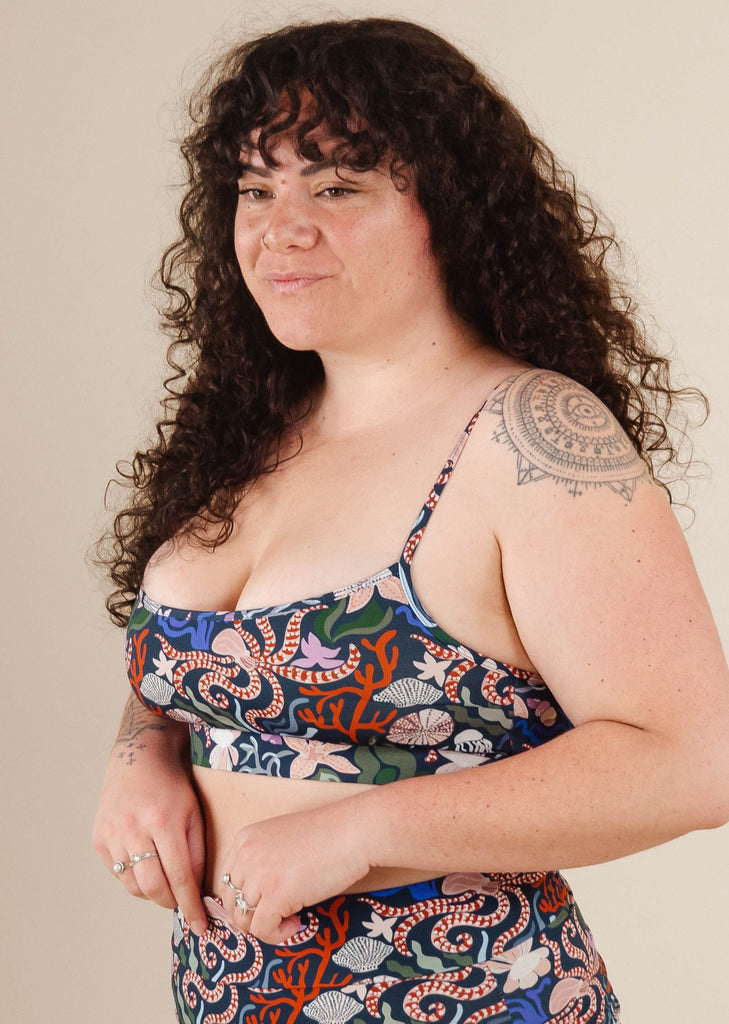 Une femme avec un tatouage sur le bras posant pour une photo dans le haut de bikini Mimi et august Oceana Bralette Mango.