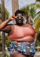 Une femme souriante sur la plage de Miami portant un haut de bikini Mimi et august Sunset Bralette de Mango et un bas de bikini à fleurs.