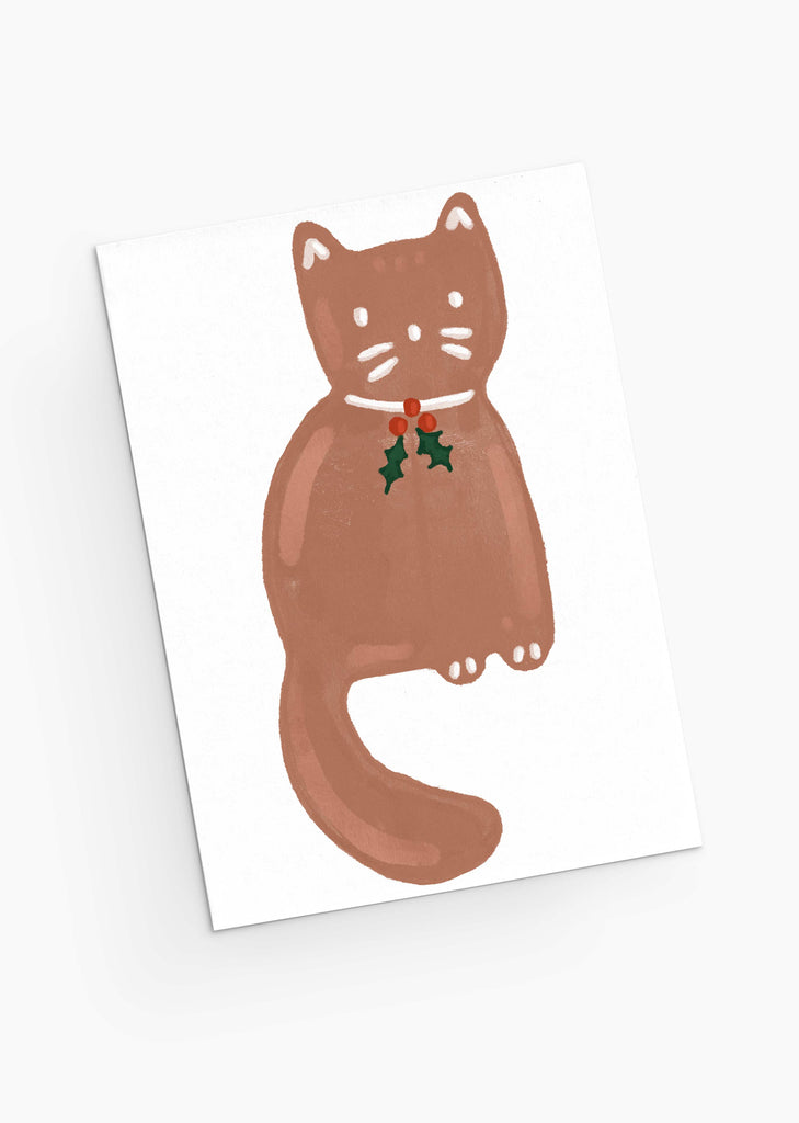 The "Merry Cookie - Christmas Greeting Card" by Mimi & August features an illustration of a brown cat with a red collar and holly leaves, sitting on a white background. It's perfect for holiday greetings and printed on recycled paper.