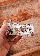 A hand holds a rectangular Mimi & August “Mimi Floral Matchbox - 30 Sticks” over a wooden surface, displaying its decorative matches inside.