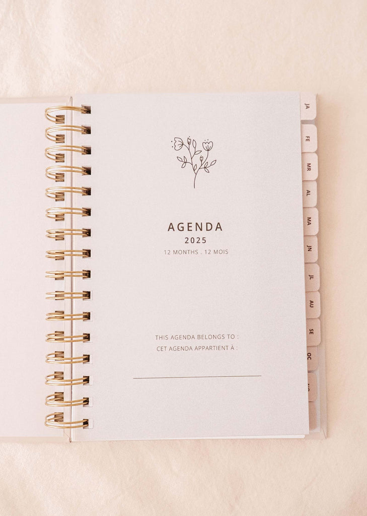 Explore the Les Oranges - Agenda 2025 by Mimi & August, a planner featuring a lively hand-drawn orange fruit design on the cover, equipped with a spiral binding and handy labeled monthly tabs on the right.