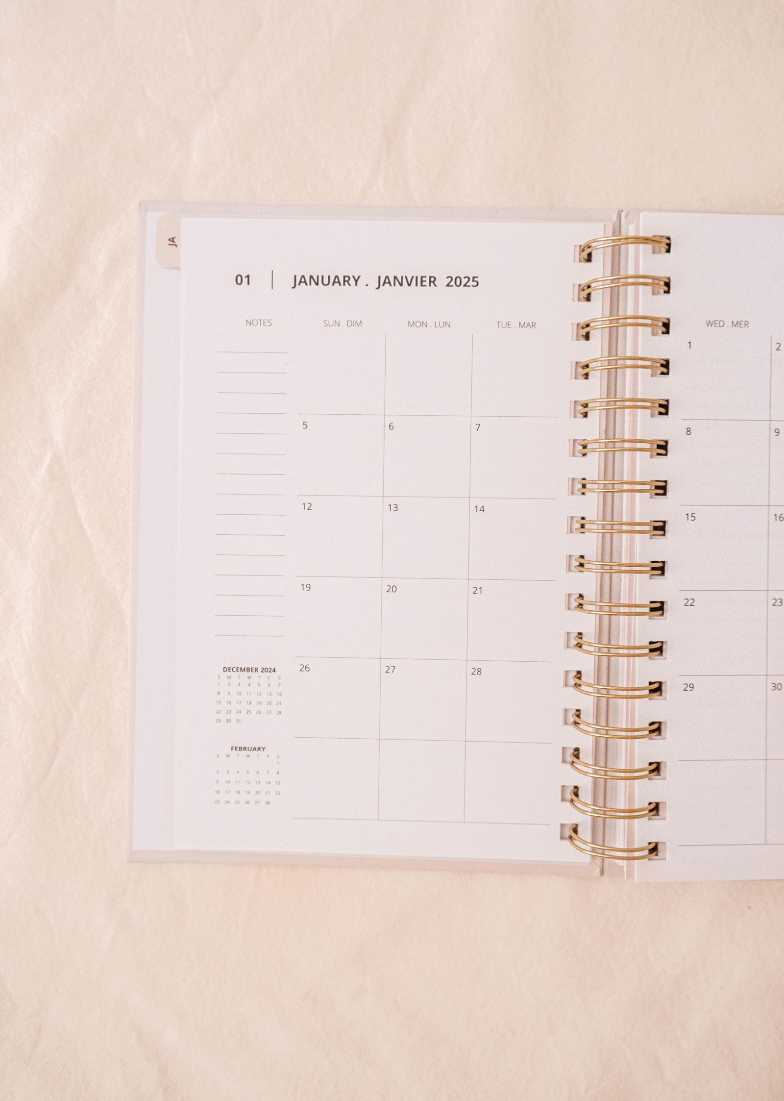 An open spiral-bound planner, the Mimi & August Lemon - Agenda 2025, lies on a light fabric surface. The January 2025 calendar is visible, adorned with a delightful hand-drawn lemon pattern.