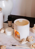 The Mimi & August Mini Aroma Diffuser sits on a marble surface, surrounded by wax melts, dried flowers, and two small essential oil bottles.