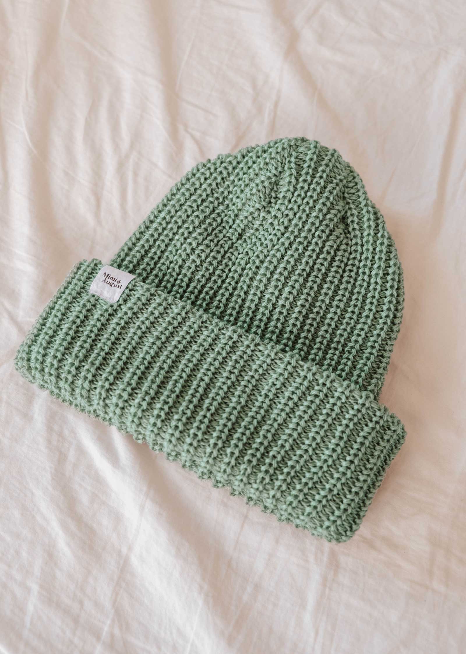 Véritable indispensable de l'hiver, le bonnet Mist Chunky Beanie de Mimi & August se décline dans une douce couleur brumeuse et comporte une petite étiquette blanche sur le bord replié, gracieusement posée sur un fond de tissu blanc.