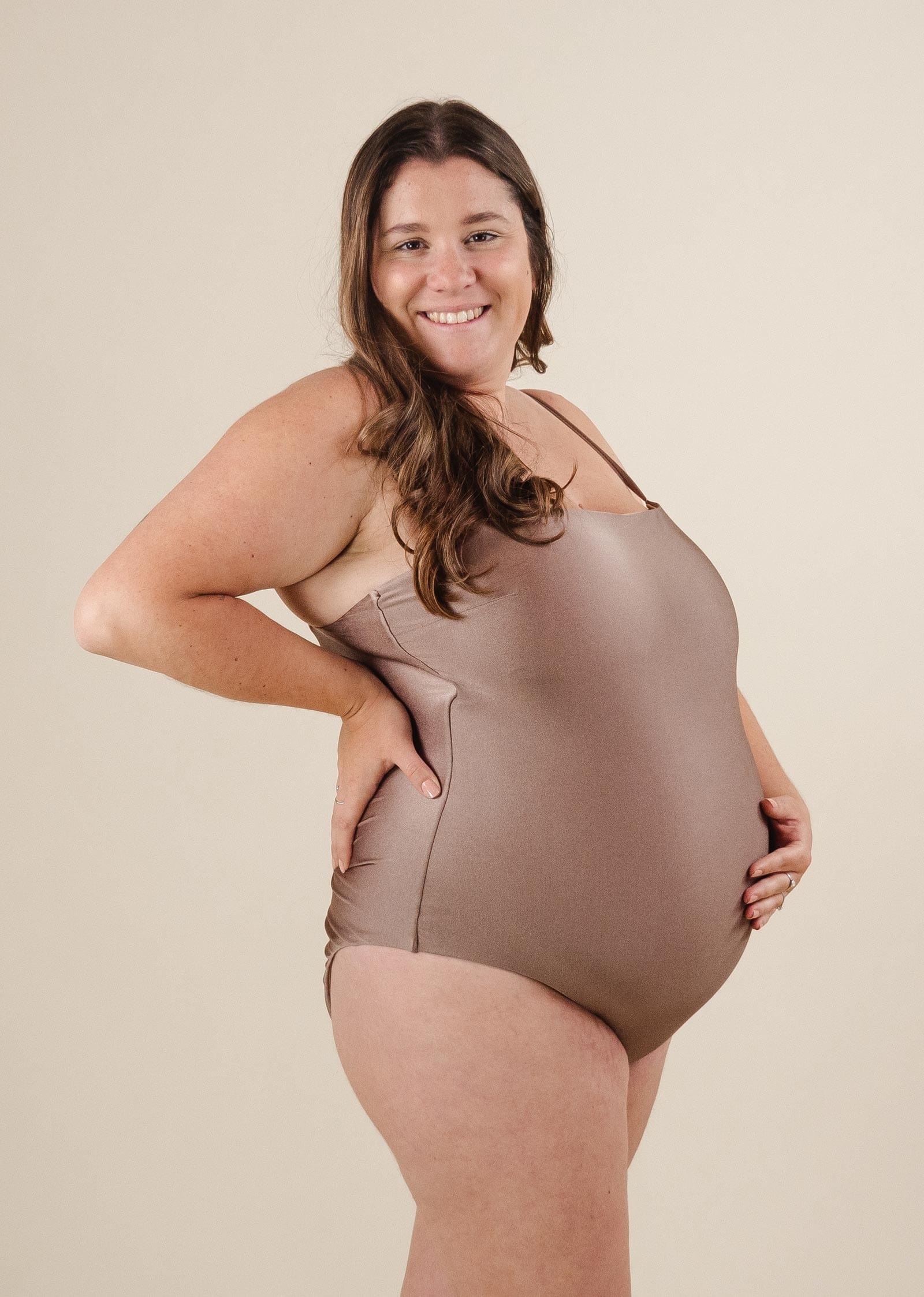 Une femme enceinte pose pour une photo avec le maillot de bain une pièce Nohea Dunes de mimi et august.