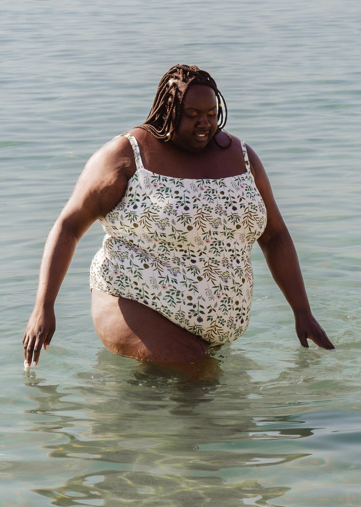 A plus size woman standing on the beach in a Nohea Herboria One-Piece Swimsuit.
