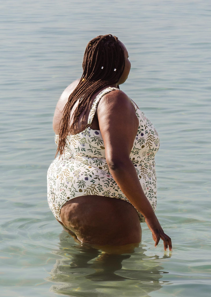 A woman kneeling at Miami Beach in the water wearing an Adjustable Cheeky One Piece Swimsuit.