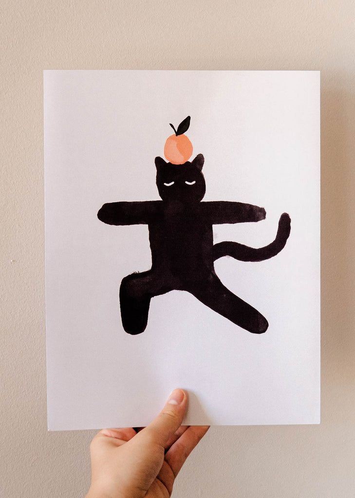 Un chat noir avec une orange imprimé par Mimi & August, parfait pour les amoureux des chats.