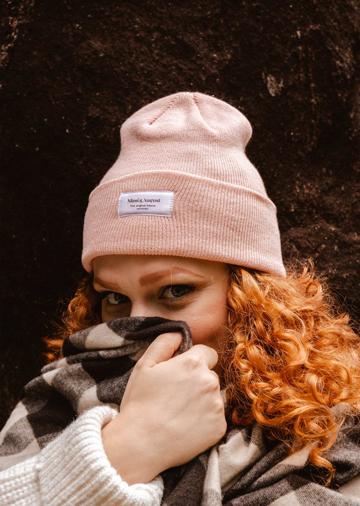 A woman wearing a Pale Rose Beanie and plaid blanket.