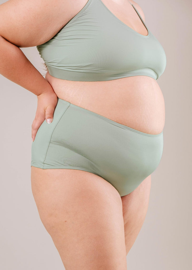 A side view of a plus-size woman wearing a Paloma Agave High Waist Bikini Bottom in turquoise green, emphasizing body positivity, by Mimi & August.