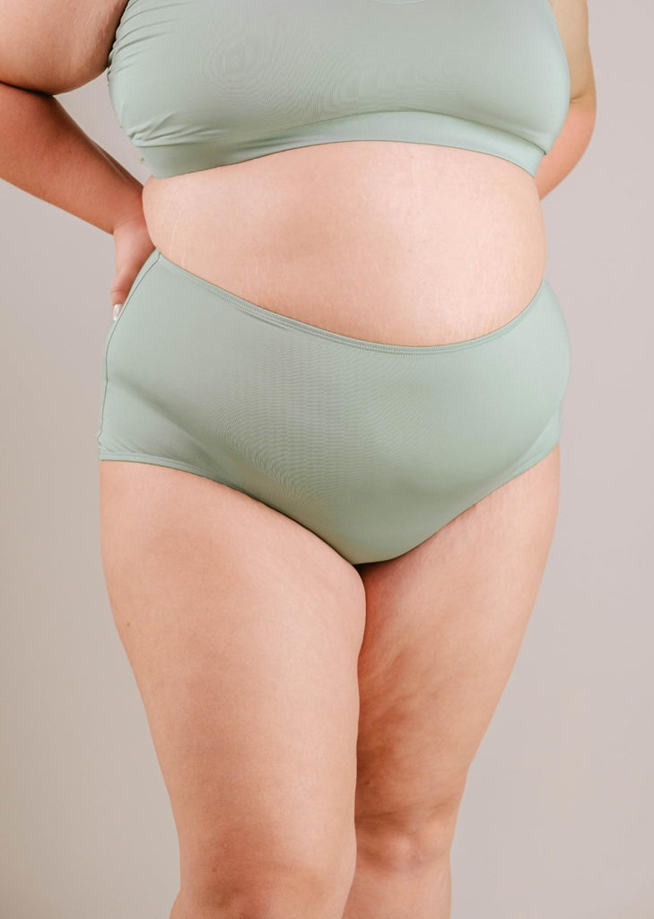 A close-up of a woman wearing the Mimi & August Paloma Agave High Waist Bikini Bottom, showing her midsection and thighs against a neutral background.