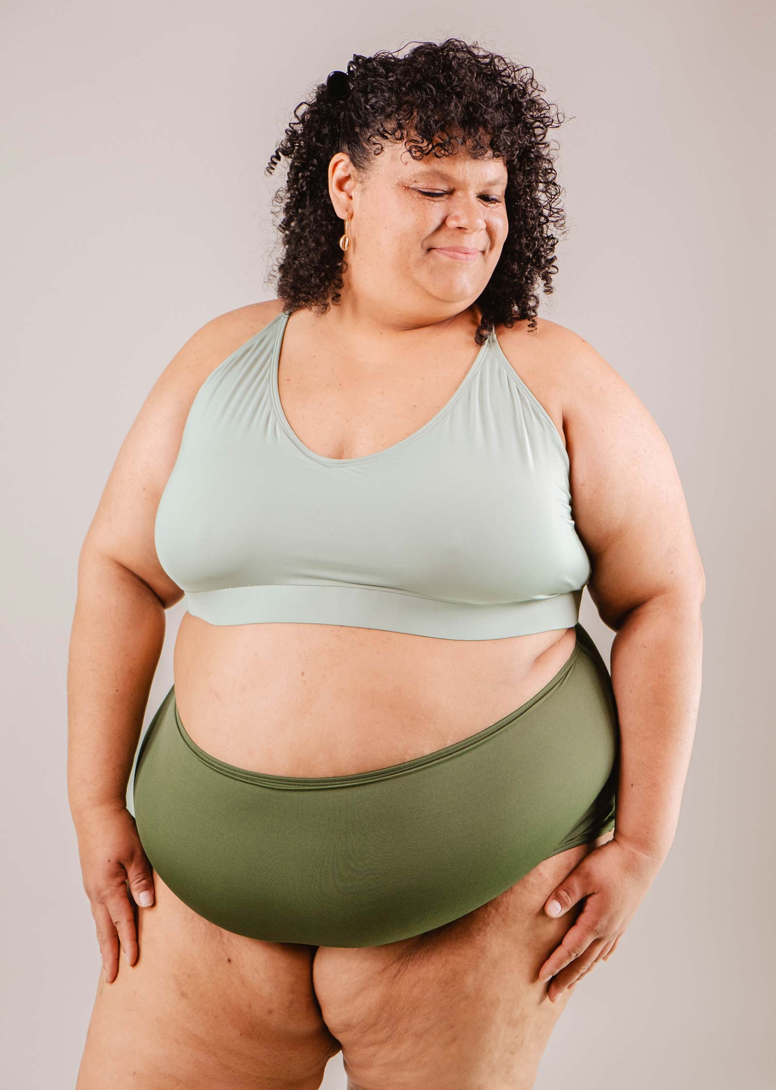 A woman wearing a Paloma Amazonia high-waist bikini bottom and matching sports bra from Mimi & August, standing confidently against a neutral background.