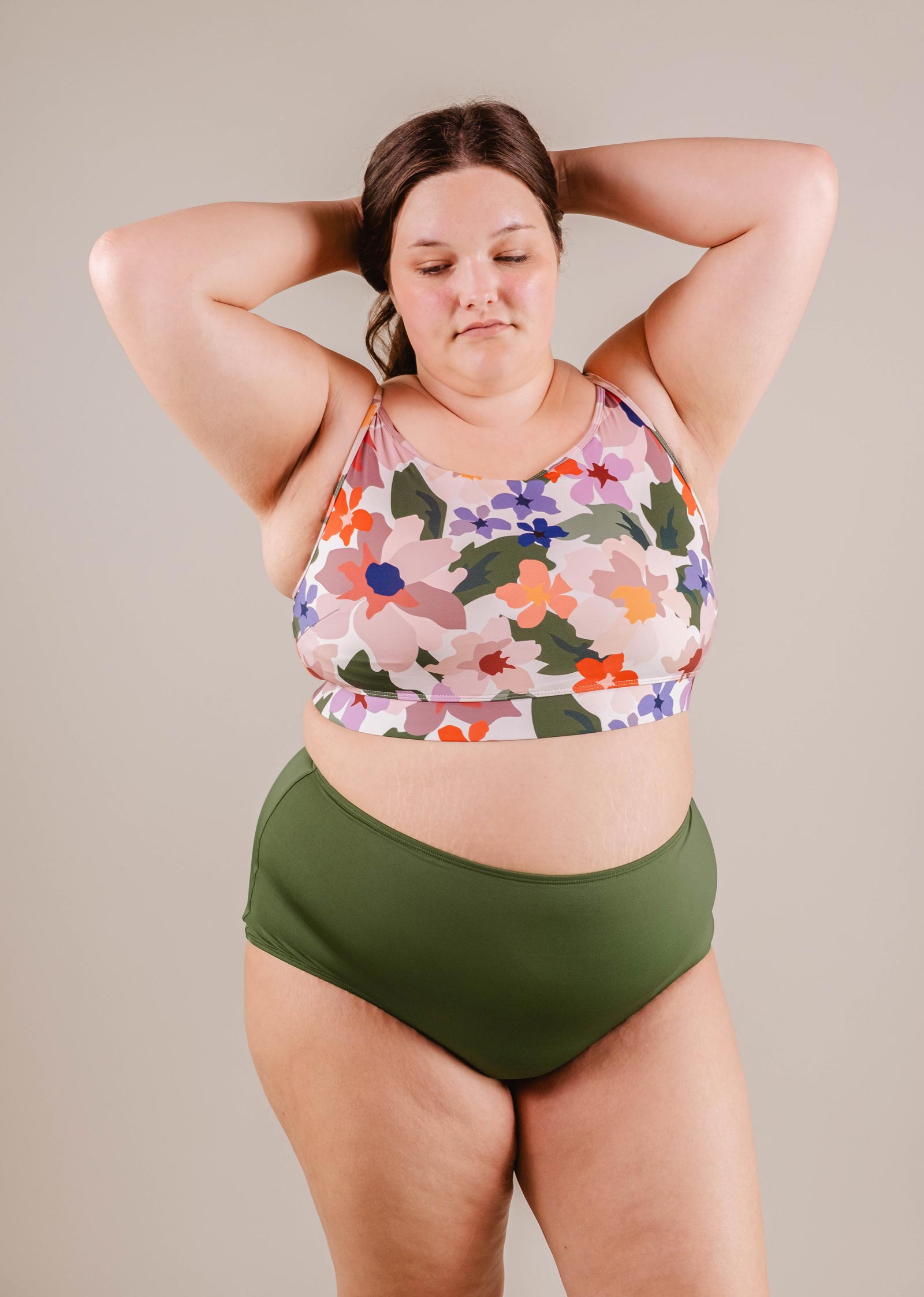 A plus-size woman in a floral bikini top and Mimi & August Paloma Amazonia high-waist bikini bottoms stands confidently against a neutral background.