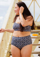 Une femme vêtue d'un bas de bikini taille haute et d'un haut de bikini Mimi and August Paloma Moonflower, debout sur un escalier.